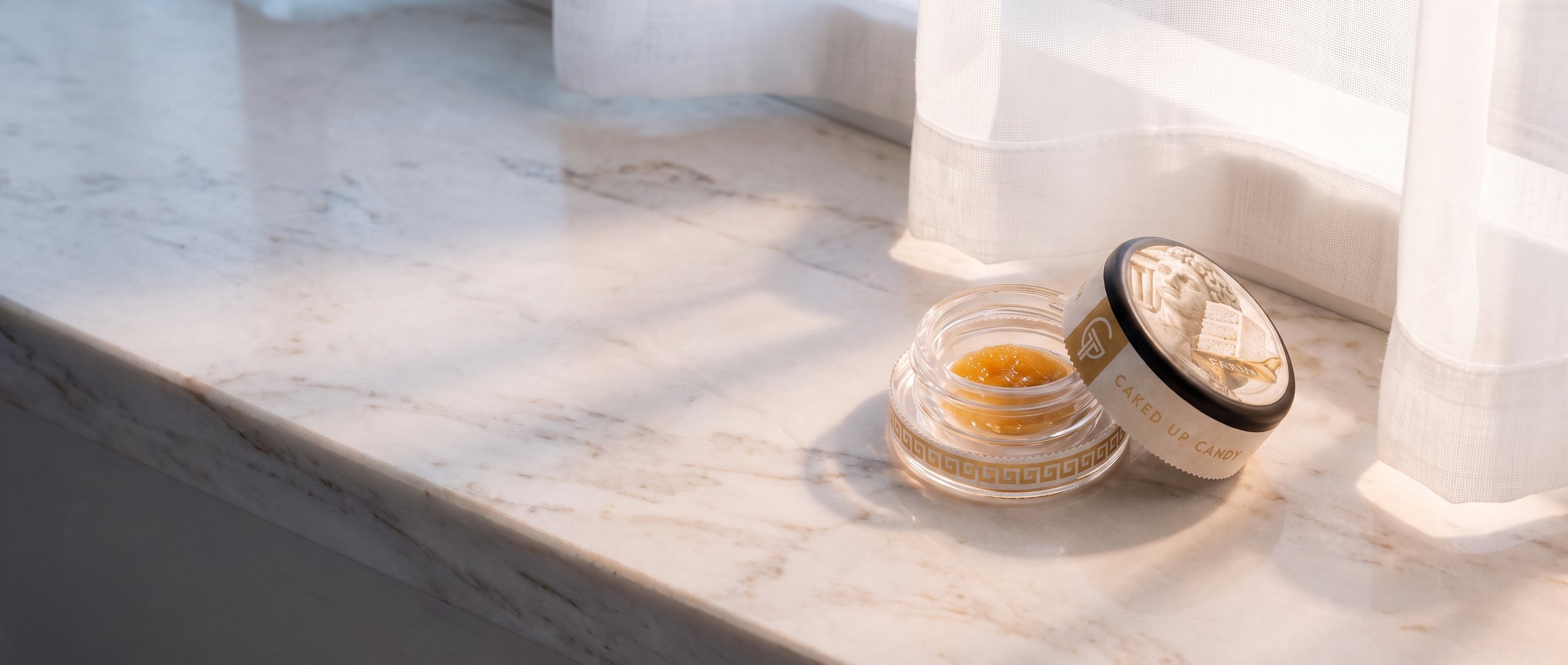 An open Caked Up Candy jar in morning light on a marble sill